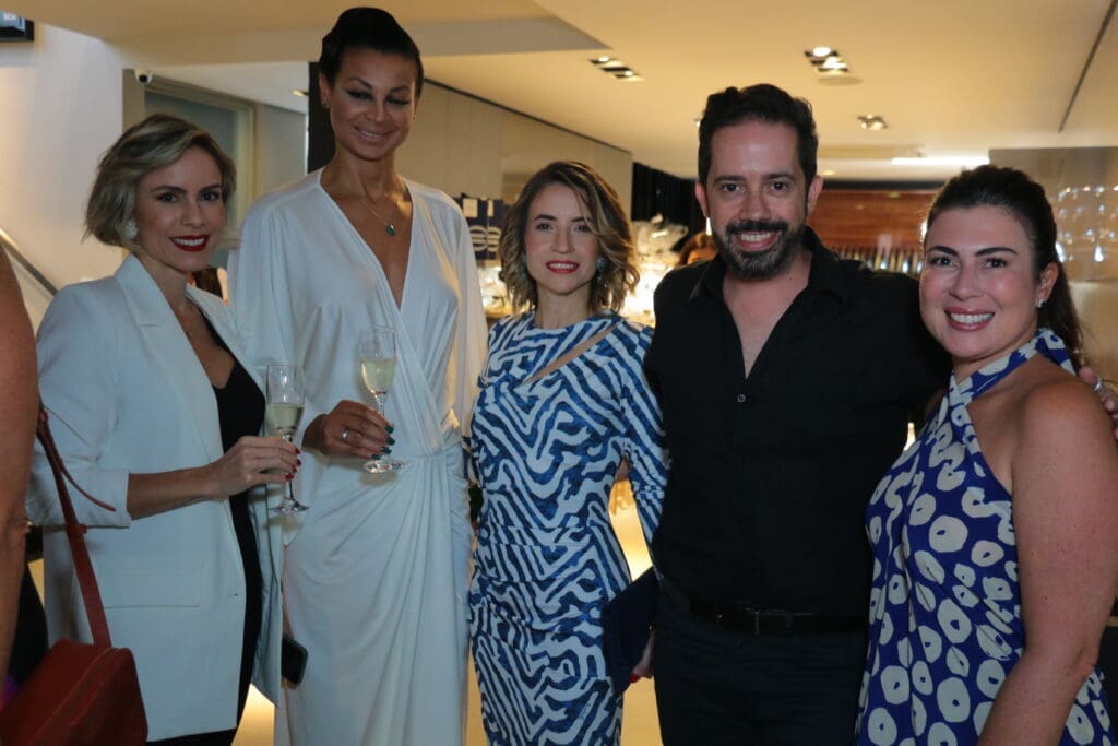 Quatro mulheres e um homem vestidso com roupas elegantes de festa sorrindo para foto.