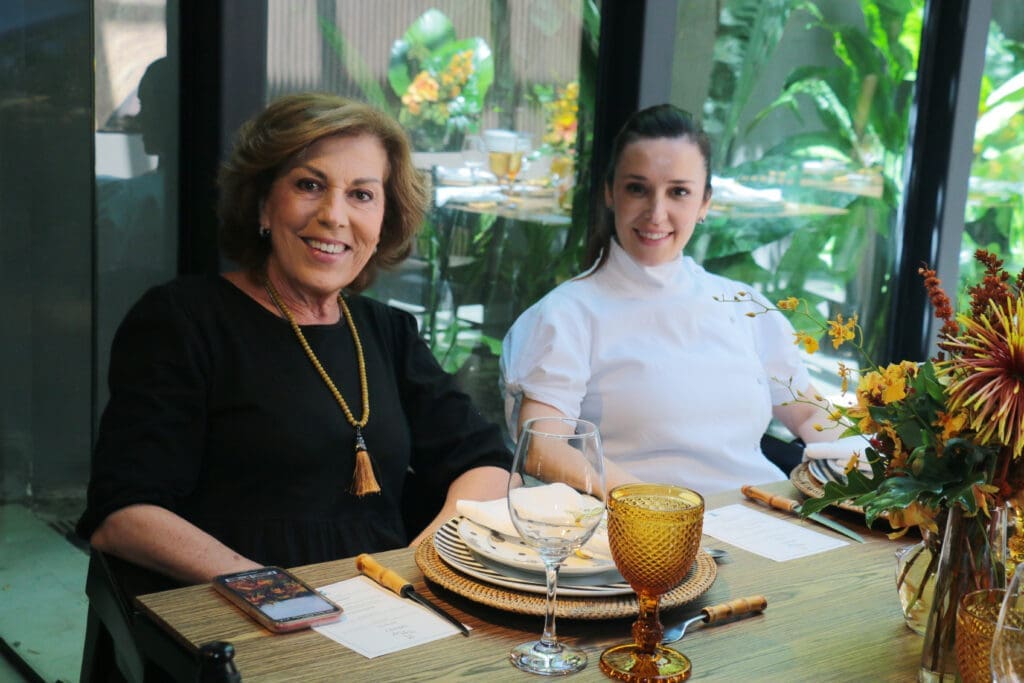 Duas mulheres sentada á mesa sorrindo