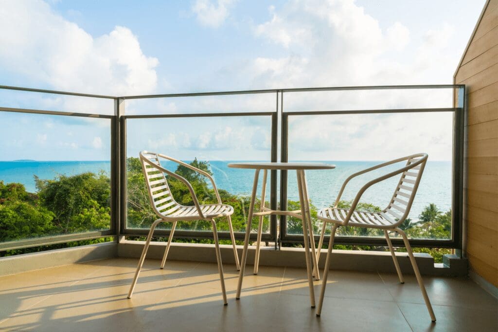 Imagem de uma sacada, com vista para o mar com duas cadeiras e uma pequena mesa