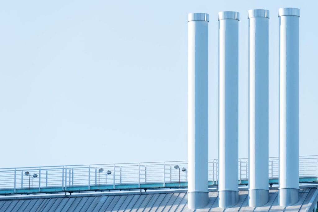Quatro grandes dutos industriais verticais em estrutura metálica sobre o telhado de uma instalação moderna, representando sistemas de ventilação, exaustão ou climatização em projetos Built to Suit (BTS) para o setor de energia, óleo e gás, com foco em eficiência operacional e soluções sustentáveis.