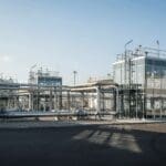 Complexo industrial moderno com estruturas envidraçadas, tubulações e tanques de armazenamento, representando projetos Built to Suit (BTS) no setor de óleo, gás e energia, com destaque para eficiência, tecnologia e integração de fontes renováveis.