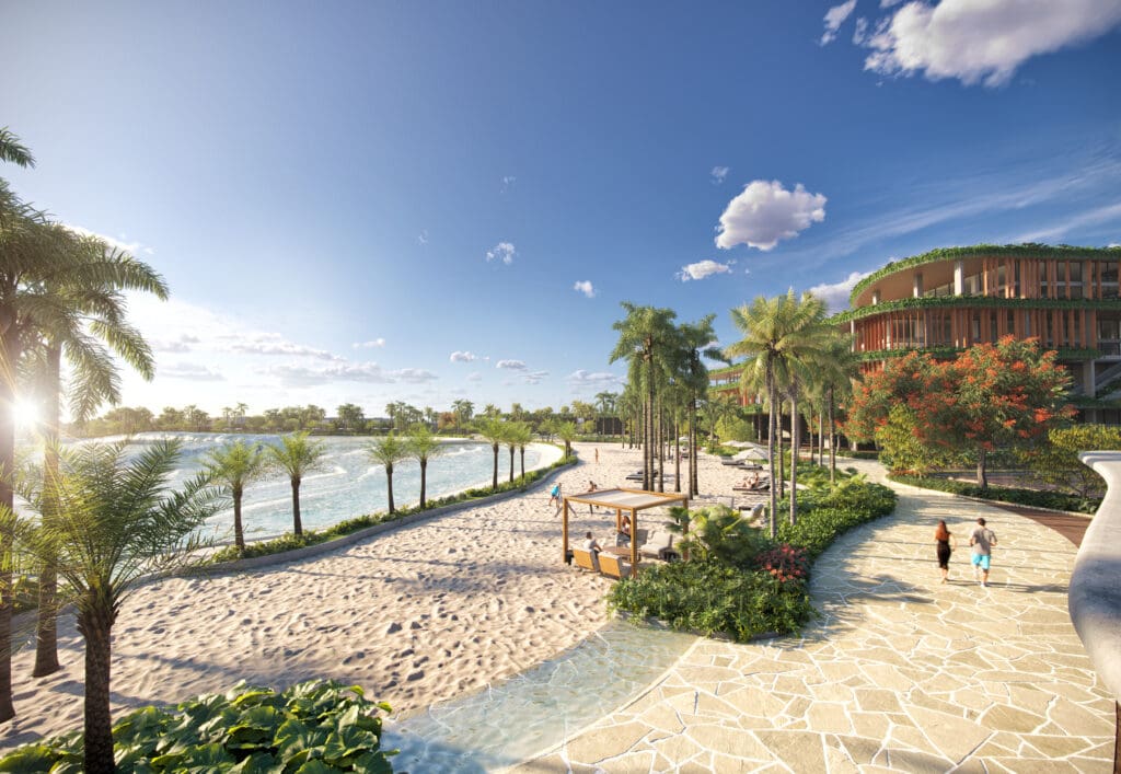 Vista de praia artificial com areia branca, palmeiras, lago de ondas e pessoas caminhando em calçadão arborizado ao lado de edifício moderno com vegetação.