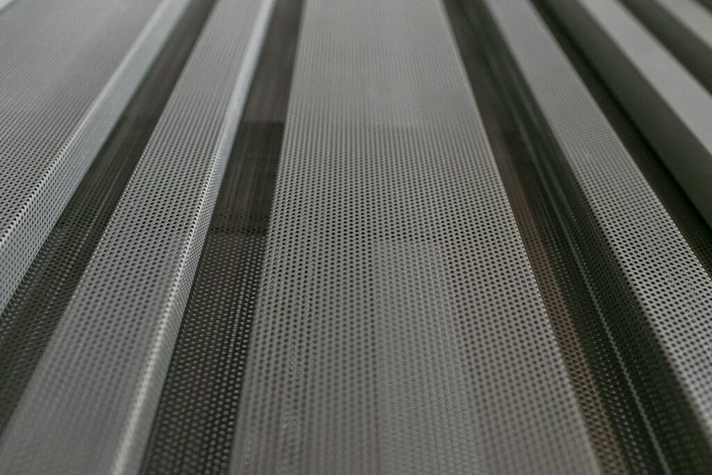 Detalhe de painéis metálicos perfurados em close, mostrando textura e padrão geométrico do revestimento.
