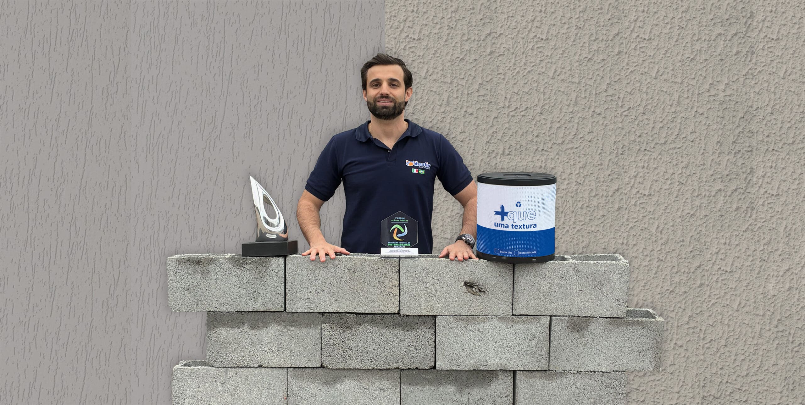 Representante da Ibratin com troféus de premiação, blocos sustentáveis e embalagem da Textura Biotex, simbolizando inovação e economia circular no setor de tintas.