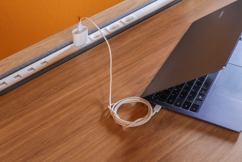 Notebook conectado a tomada embutida em estação de trabalho Novara com acabamento em madeira.