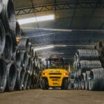 Empilhadeira movimentando bobinas de aço em galpão industrial da Udiaço, referência em corte e dobra industrializado.
