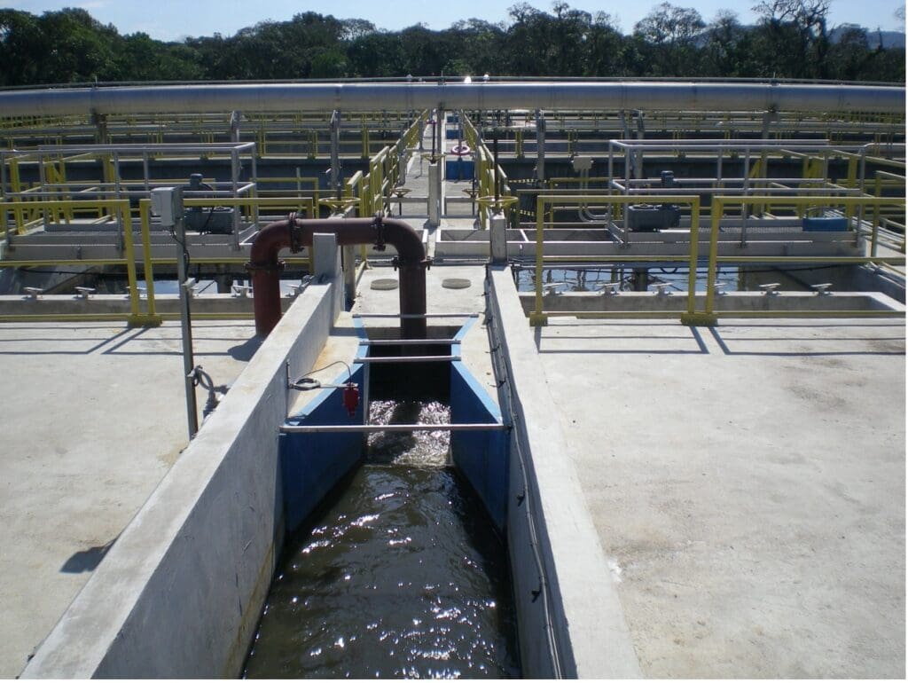 Vista de uma estação de tratamento de esgoto com estruturas de concreto e tubulações, destacando a importância da proteção antimicrobiana para durabilidade.