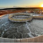 Tanque circular de tratamento de efluentes industriais ao entardecer, destacando a importância da proteção antimicrobiana no saneamento.