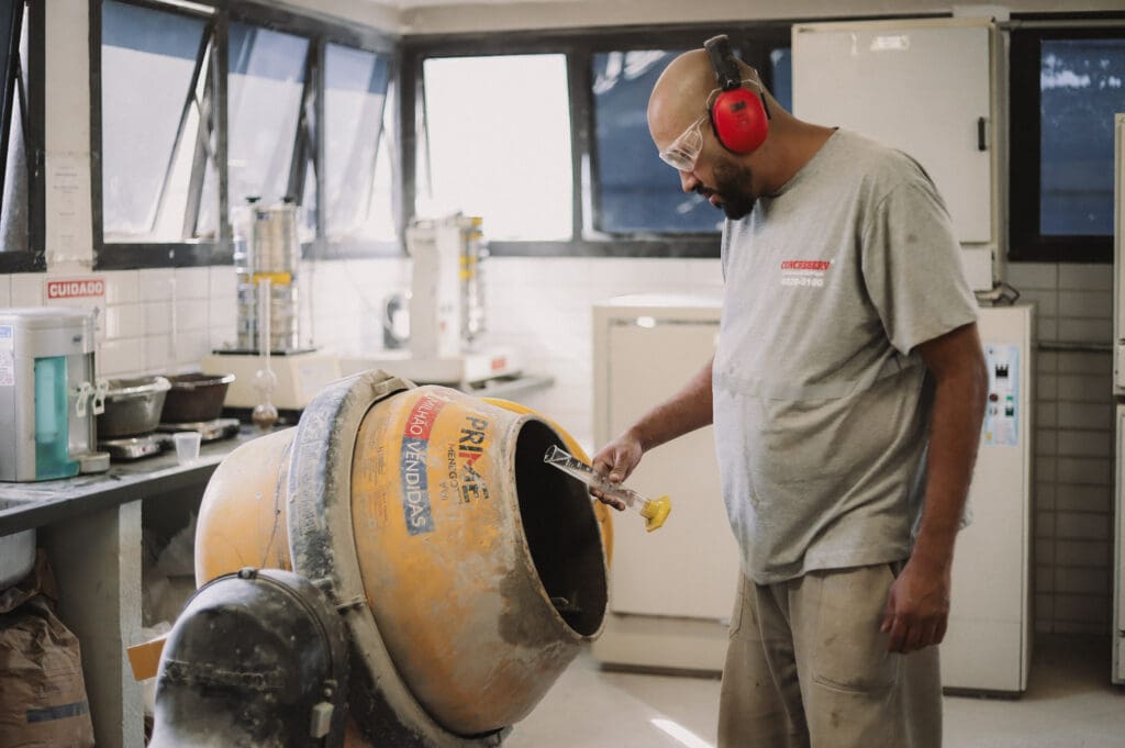 Colaborador da Concreserv utilizando betoneira em laboratório para testes de qualidade do concreto, com equipamentos de proteção individual e ambiente controlado.
