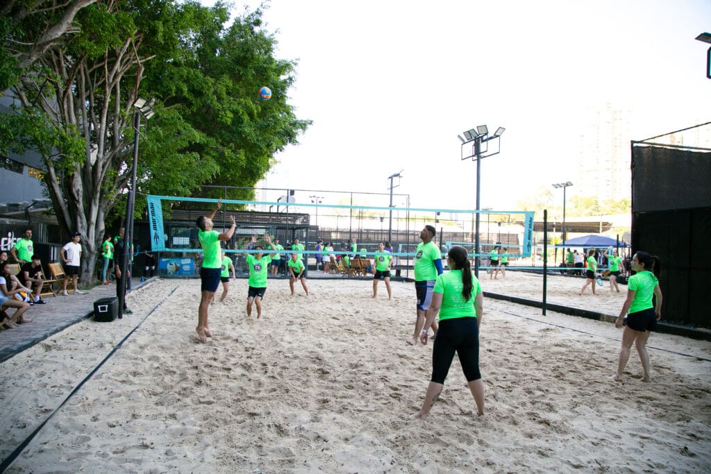 Atletas com camisetas verdes disputam partida de vôlei de praia durante o 3º C3 Open Beach Sports, em quadra de areia ao ar livre.