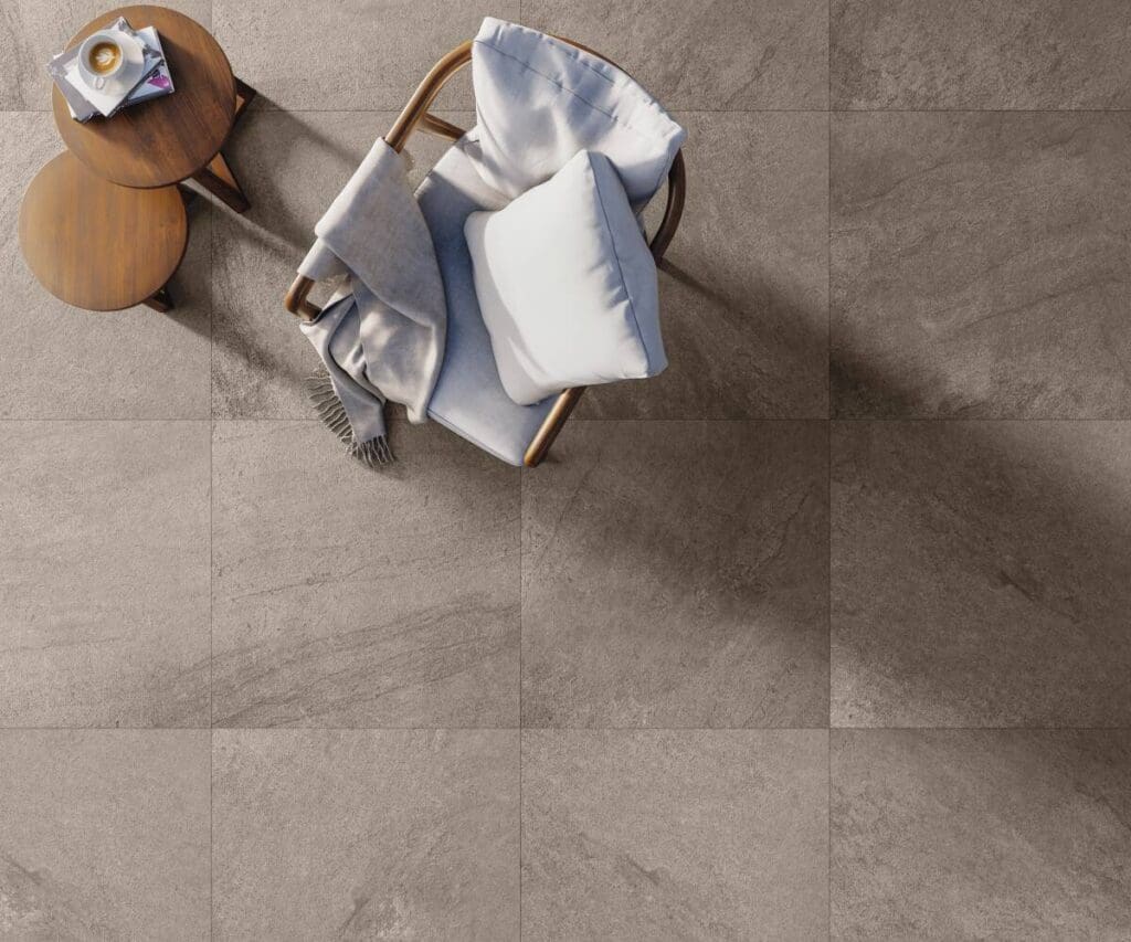 Ambiente com piso porcelanato Portobello Thor Amber 81x81 cm, poltrona com manta e almofada, e mesas de apoio, destacando conforto e sofisticação.