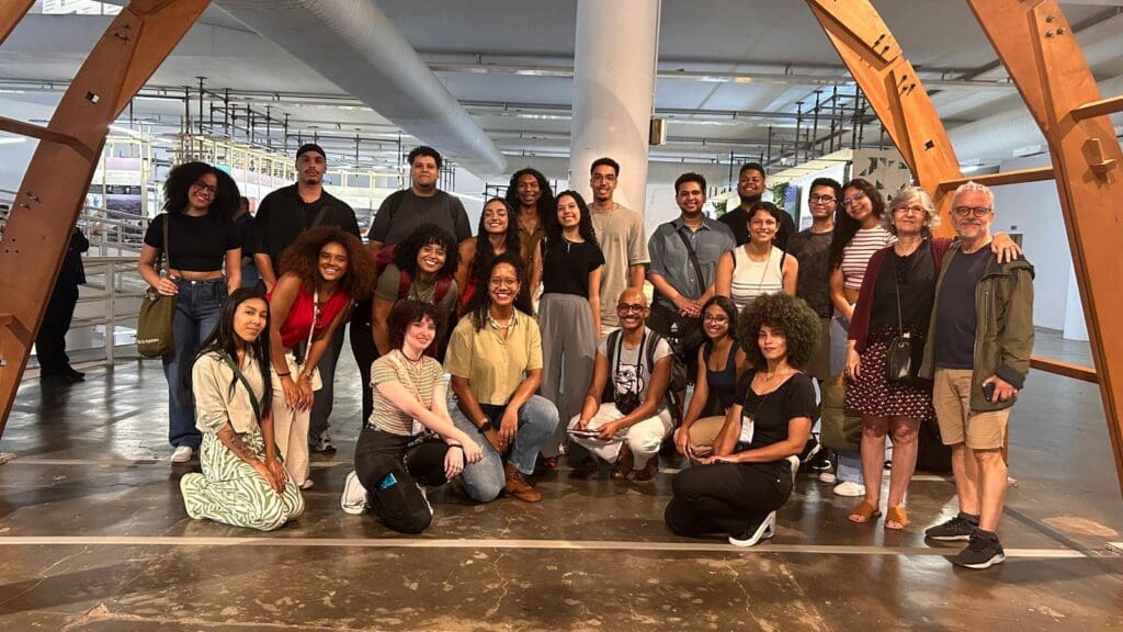 Grupo diverso de estudantes e mentores do Programa Aproxima posando juntos em espaço cultural, destacando a inclusão étnico-racial na arquitetura.