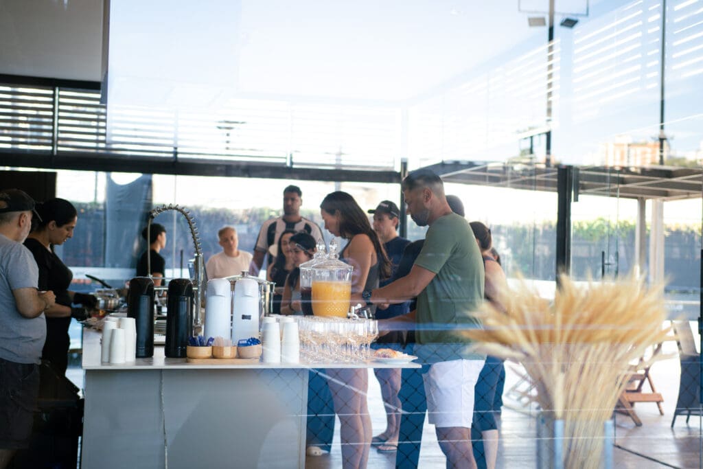Participantes do 3º C3 Open Beach Sports se servem no Espaço Gourmet, desfrutando de opções gastronômicas em ambiente moderno e acolhedor.