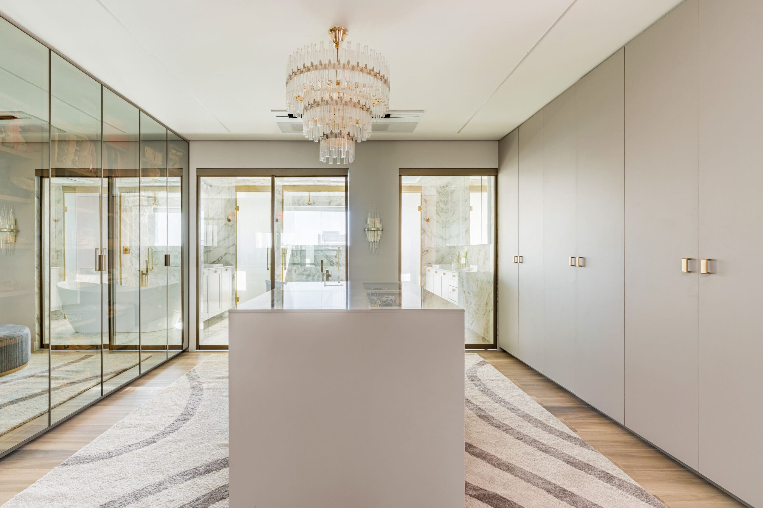 Walk-in closet sofisticado com armários espelhados, ilha central e iluminação elegante, integrado ao banheiro.