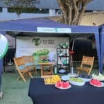 Estande do projeto “inVista no Bem” durante o C3 Open, realizado em 29 de novembro na Arena BTG, em São Paulo, com tendas, mesas de madeira, frutas frescas e painel em formato de coração.
