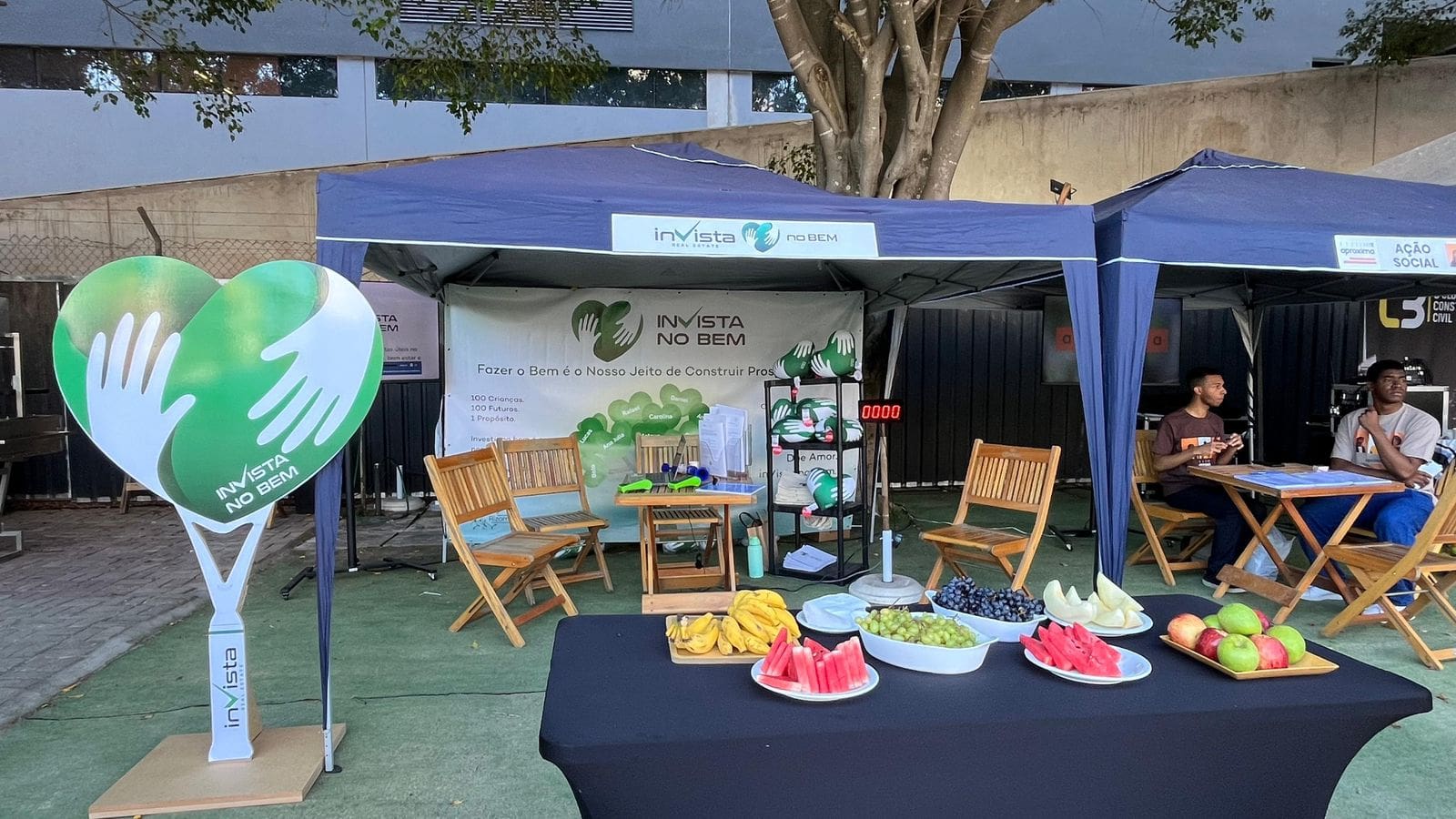 Estande do projeto “inVista no Bem” durante o C3 Open, realizado em 29 de novembro na Arena BTG, em São Paulo, com tendas, mesas de madeira, frutas frescas e painel em formato de coração.