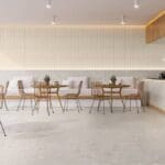 Cafeteria contemporânea com piso Portobello Lombarda Viva Avorio 120x120 cm, mesas e cadeiras de madeira, iluminação suave e decoração minimalista.