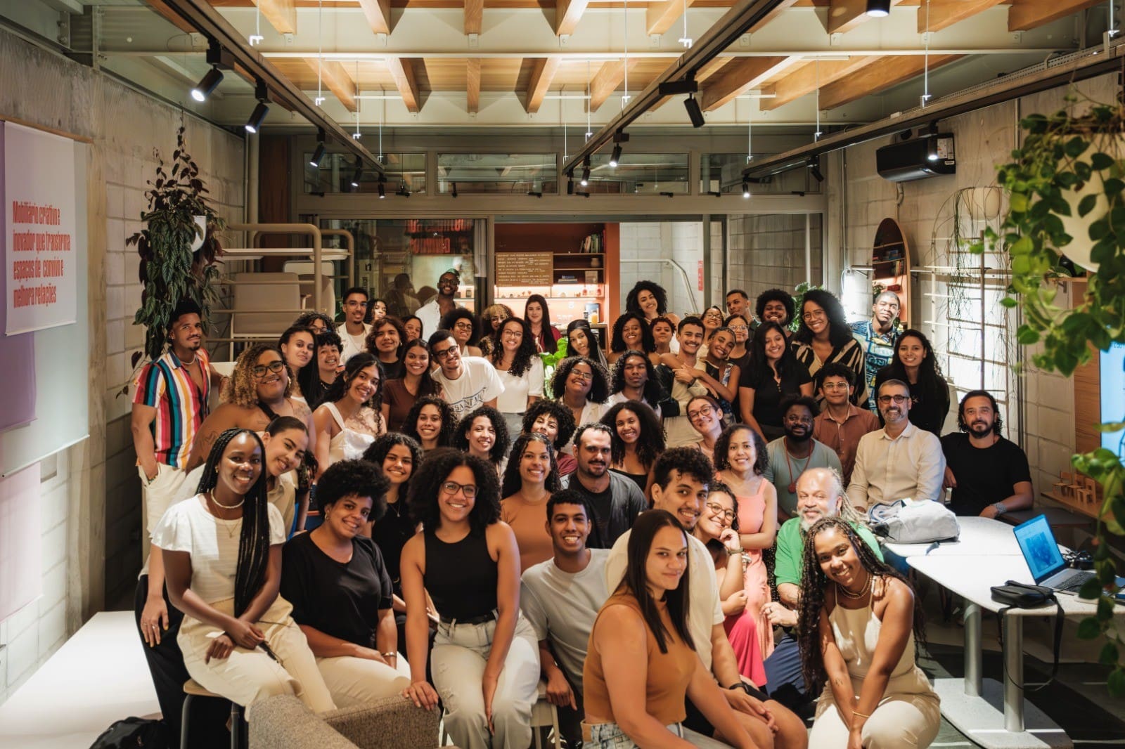 Grupo diverso de jovens estudantes e profissionais reunidos em ambiente moderno durante evento do Programa Aproxima, que promove diversidade e inclusão étnico-racial na arquitetura.