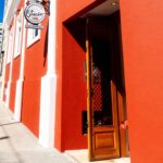 Fachada restaurada de um edifício histórico com pintura vermelha e detalhes brancos, abrigando um restaurante, em área urbana revitalizada.