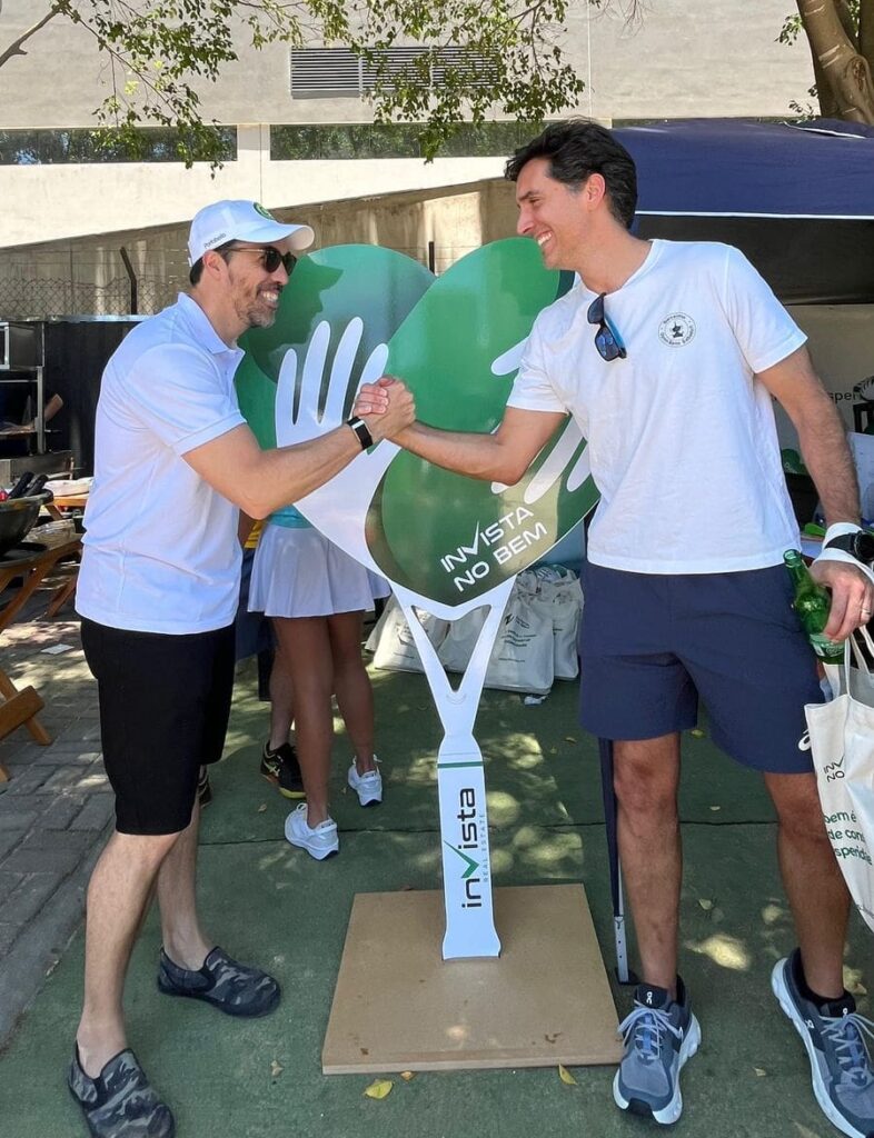 Dois participantes do C3 Open cumprimentam-se sorrindo em frente ao totem do projeto “inVista no Bem”, durante o evento realizado em 29 de novembro na Arena BTG, em São Paulo.