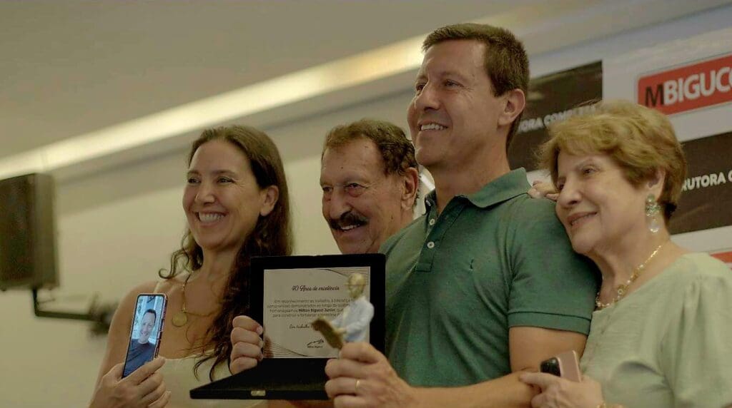 Milton Bigucci Junior sorri ao segurar uma placa de homenagem pelos seus 40 anos de carreira, acompanhado por familiares durante evento da construtora MBigucci.