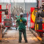 Colaborador da Udiaço opera maquinário de corte e dobra de aço em ambiente industrial moderno, com equipamentos de alta tecnologia e segurança.