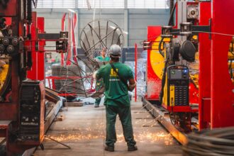 Colaborador da Udiaço opera maquinário de corte e dobra de aço em ambiente industrial moderno, com equipamentos de alta tecnologia e segurança.