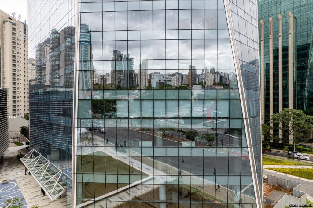 Close lateral da fachada do Edifício Birmann 32, mostrando o reflexo nítido de prédios vizinhos e da rua na pele de vidro Neutral Plus 50 da Guardian Glass.