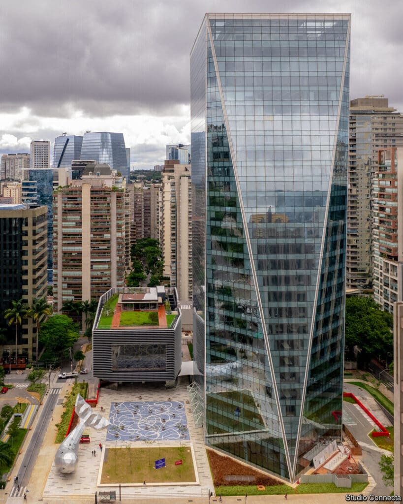 Vista aérea vertical do Edifício Birmann 32 evidenciando o design da fachada envidraçada, o teto verde do Teatro B32 e a escultura da baleia na praça central.