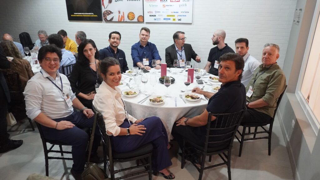 Profissionais da construção civil sentados ao redor de uma mesa redonda durante o 59° Almoço de Negócios C3, sorrindo e interagindo em ambiente de networking.