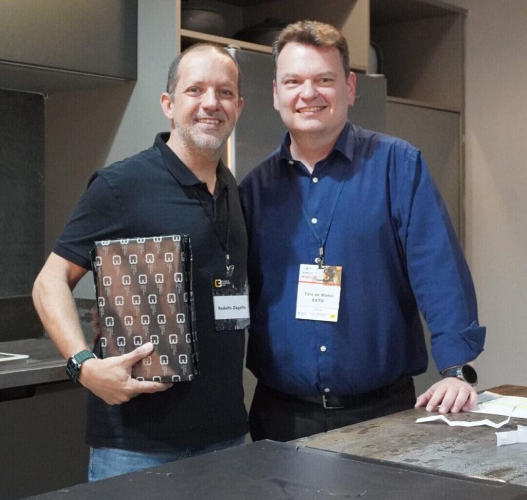 Tillo de Matos, da Exto, recebe prêmio da Dlock Hospitality durante sorteio especial no 59° Almoço de Negócios C3, simbolizando inovação e integração no evento.
