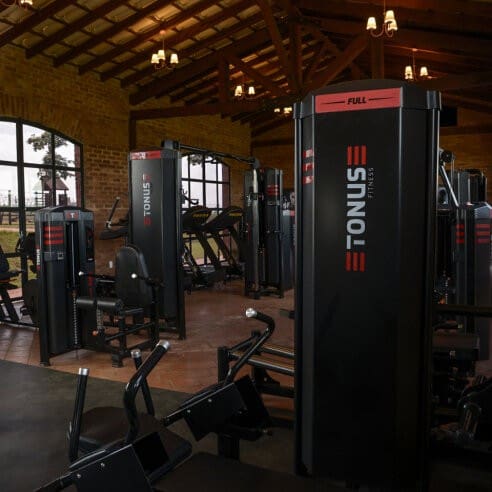 Academia do condomínio com equipamentos profissionais de musculação em ambiente amplo, com iluminação quente e layout organizado