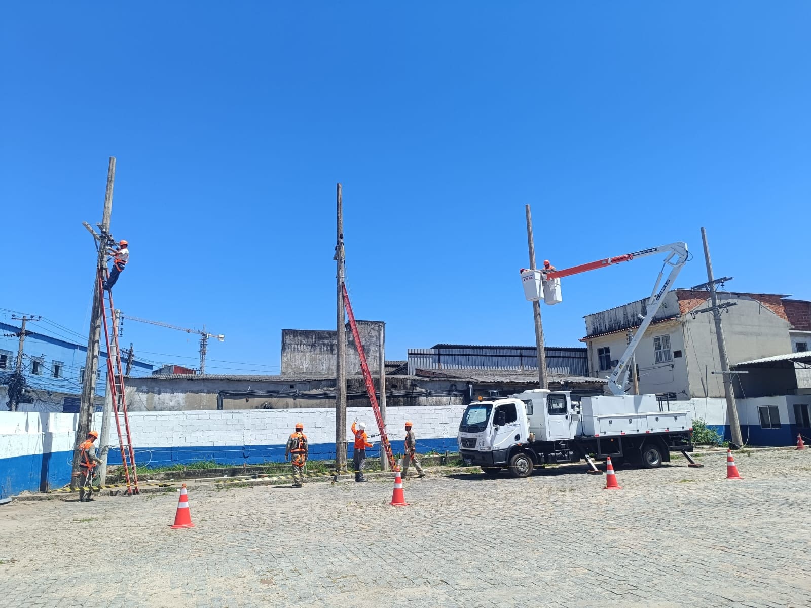 Equipe de eletricistas realiza manutenção e expansão de rede elétrica com caminhão munck e cesto aéreo em área urbana, representando operações da Light Energia.