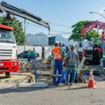 Equipe de trabalhadores da construção civil realiza obra de infraestrutura urbana com caminhões e equipamentos pesados em rua, representando o avanço das obras da Concrejato Engenharia em 2026.