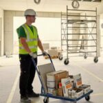 Trabalhador da construção civil transportando materiais em carrinho de abastecimento em canteiro de obras organizado, ilustrando logística lean.