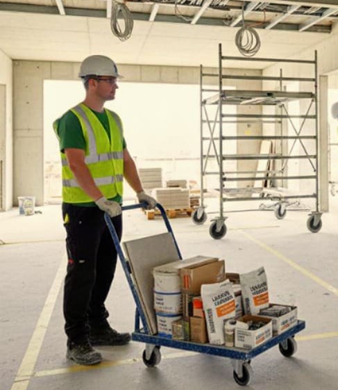 Trabalhador da construção civil transportando materiais em carrinho de abastecimento em canteiro de obras organizado, ilustrando logística lean.