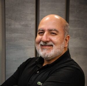 Paulo Oliveira, engenheiro civil e referência em industrialização da construção, sorrindo com os braços cruzados em ambiente corporativo.