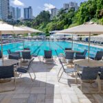 Área de piscina do Yacht Clube da Bahia com mesas, cadeiras e ombrelones Tidelli revitalizados, destacando o retrofit de mobiliário outdoor em ambiente sofisticado.
