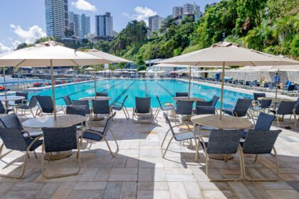 Área de piscina do Yacht Clube da Bahia com mesas, cadeiras e ombrelones Tidelli revitalizados, destacando o retrofit de mobiliário outdoor em ambiente sofisticado.