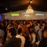 Convidados do setor da construção civil participam do coquetel de recepção do Gourmet Immersive Experience C3 no Villa Glam, com ambiente sofisticado, iluminação especial e logomarcas de patrocinadores projetadas nas paredes.