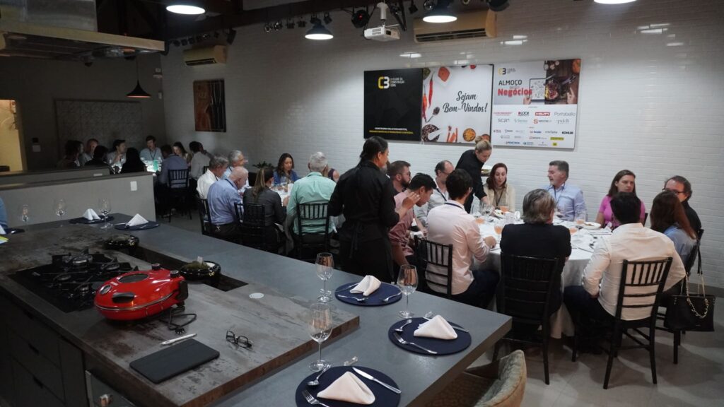 Profissionais da construção civil participam do 60° Almoço de Negócios C3, sentados em mesas redondas e interagindo em ambiente moderno no Experience Lounge, em São Paulo.