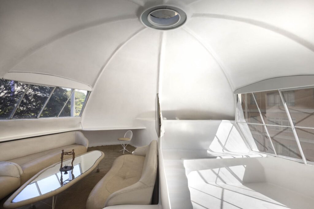 Interior futurista e iluminado da Casa Bola, com móveis integrados, paredes curvas brancas e amplas janelas, projetado por Eduardo Longo em São Paulo.