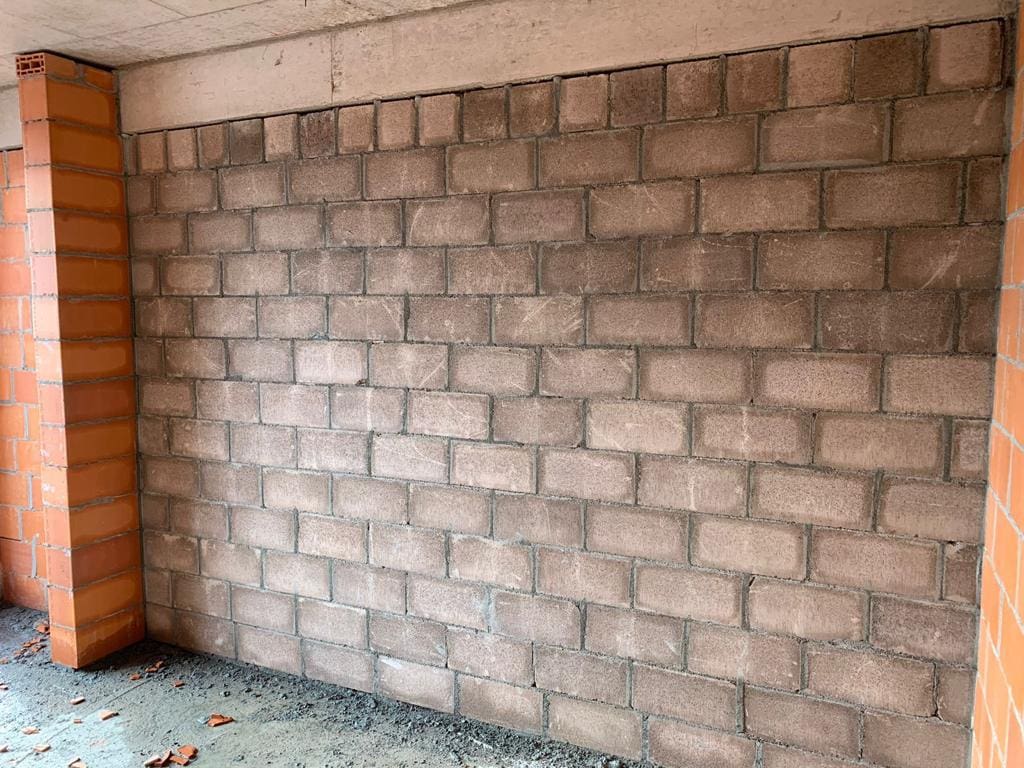Parede de blocos estruturais de concreto finalizada em obra, com pilares de tijolos cerâmicos nas laterais, evidenciando a robustez do sistema construtivo.