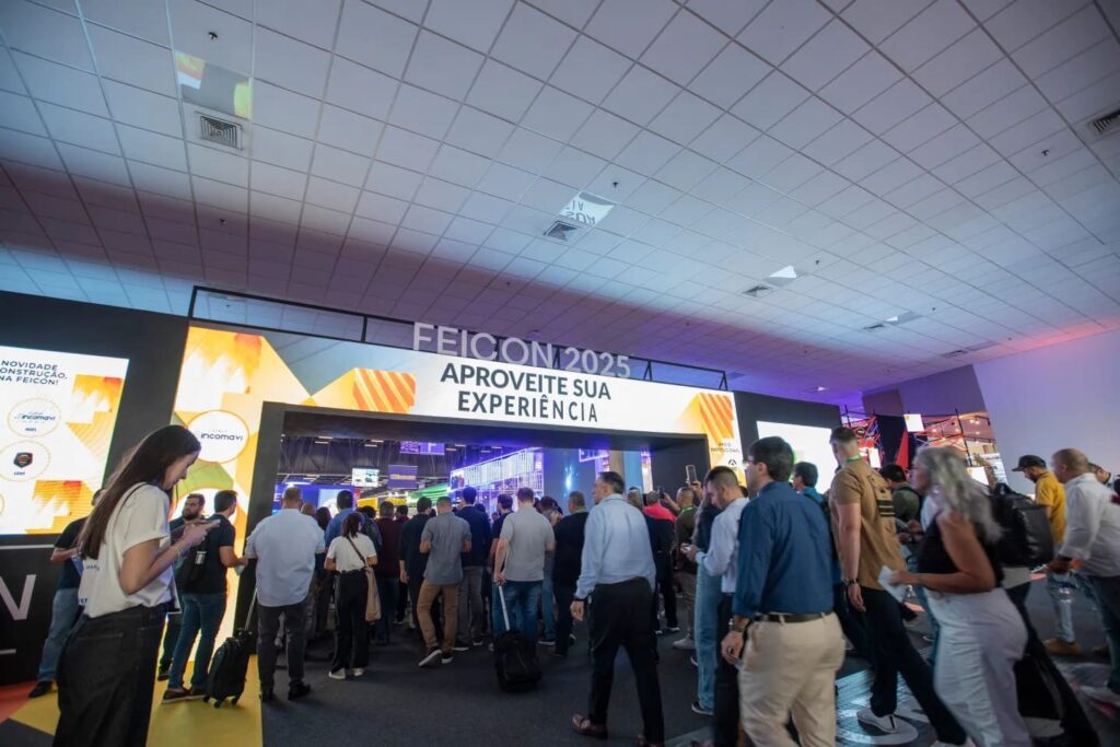 Visitantes entrando pelo portal de acesso principal da FEICON, com destaque para a mensagem “Aproveite sua experiência” e grande fluxo de pessoas no início do evento.