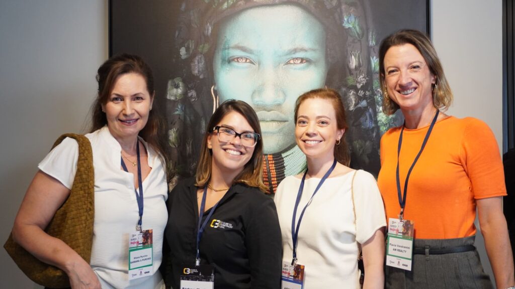 Milena Purchio, Bárbara Martinez, Juliana Zogbi e Flávia Vendramini posam sorrindo durante o 62° Almoço de Negócios C3, em frente a uma obra de arte.