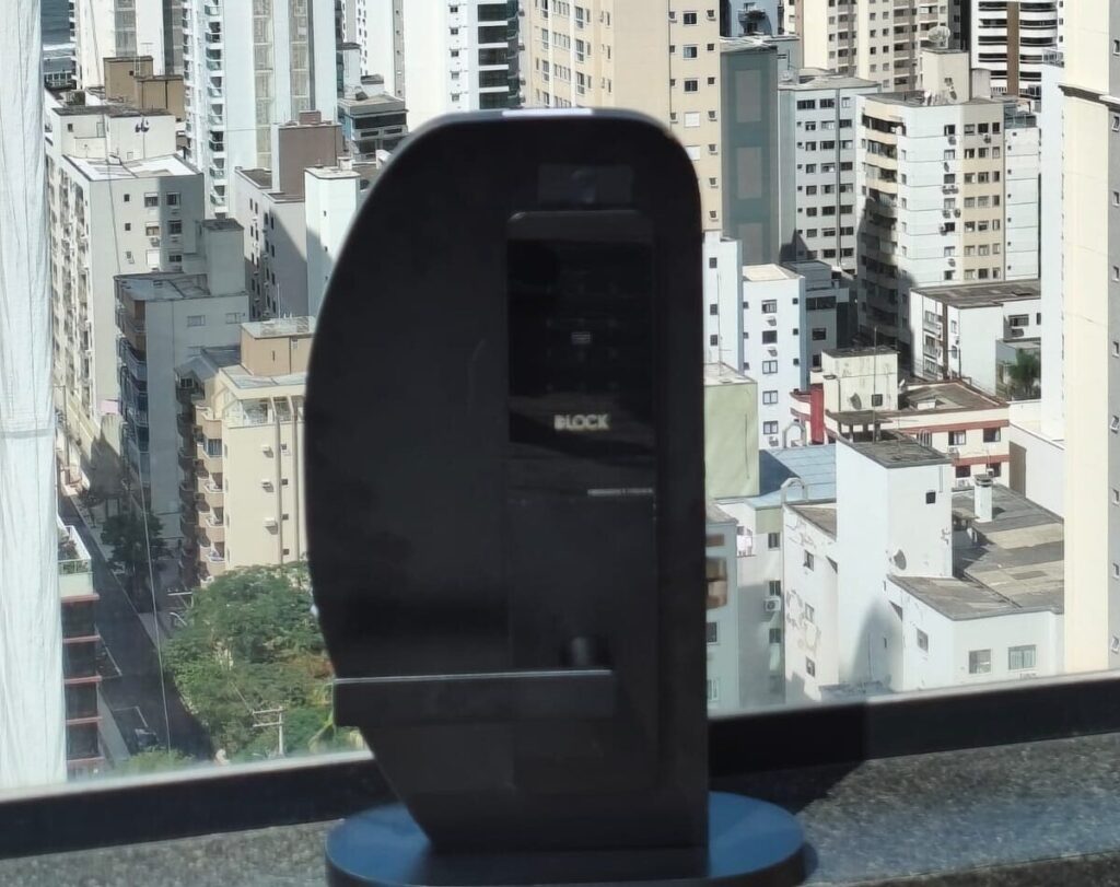 Fechadura eletrônica DLH 5700 C da DLock Hospitality exposta em frente a uma janela com vista para prédios altos em cidade litorânea.
