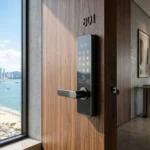 Fechadura eletrônica DLock instalada em porta de apartamento moderno com vista para a praia e skyline urbano ao fundo. Imagem Ilustrativa criada pela Equipe C3