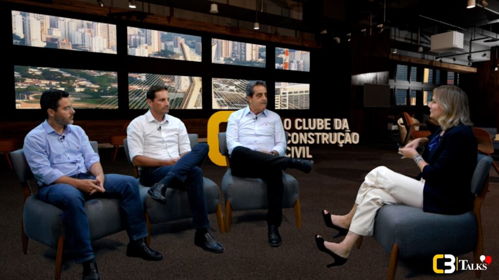 Mario Rocha, Rodrigo Rocha e Cassio Ferro, executivos da Rocontec, participam de uma conversa presencial com Lucedile Antunes, especialista em desenvolvimento humano e liderança, no estúdio do C3 Talks. Eles estão sentados em poltronas, em ambiente moderno, com painéis mostrando a cidade ao fundo.