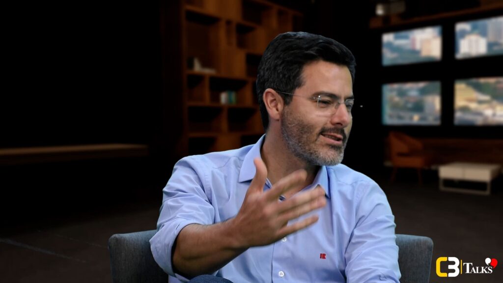 Cassio Ferro, Head de Obras Residenciais da Rocontec, participa do C3 Talks, vestindo camisa clara e microfone de lapela, em ambiente corporativo moderno.