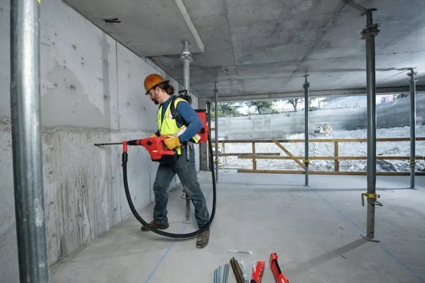 Trabalhador da construção civil utiliza martelete Hilti com sistema de extração de pó em obra, vestindo EPI completo.